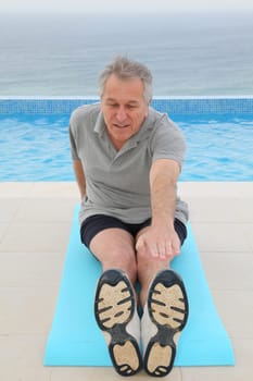 Senior man doing exercises by a swimming-pool