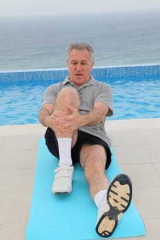 Senior man doing exercises by a swimming-pool