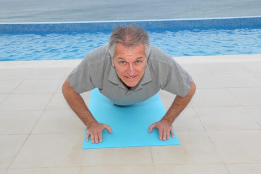Senior man doing exercises by a swimming-pool
