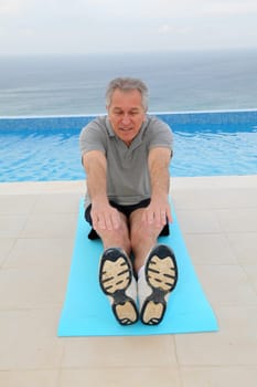 Senior man doing exercises by a swimming-pool