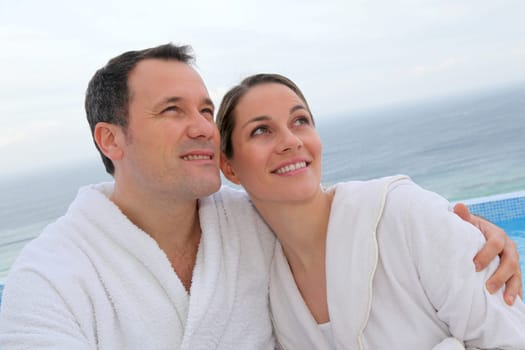 Couple in bathrobe sitting by swimming-pool