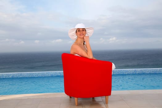 Beautiful woman relaxing in red chair by a swimming-pool