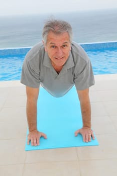 Senior man doing exercises by a swimming-pool