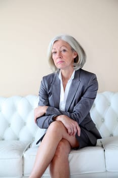 Senior woman in grey suit sitting in white sofa