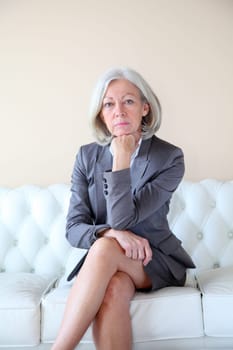 Senior woman in grey suit sitting in white sofa