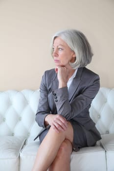 Senior woman in grey suit sitting in white sofa