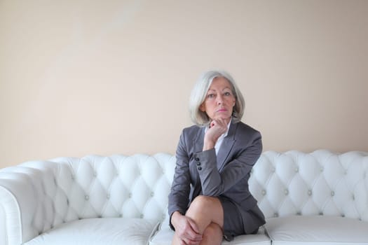 Senior woman in grey suit sitting in white sofa