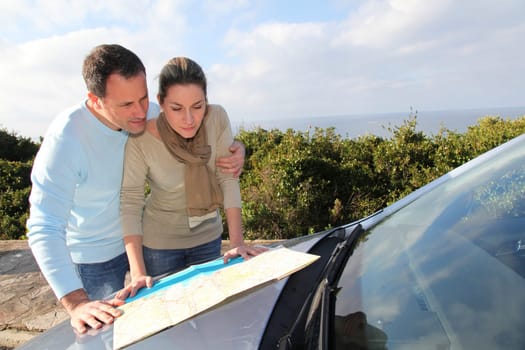 Couple looking at road map on car hood