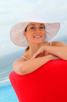 Beautiful woman relaxing in red chair by a swimming-pool