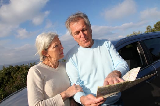 Senior couple looking at road map on car hood