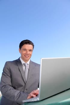 Smiling businessman working outside with laptop computer