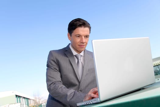 Smiling businessman working outside with laptop computer