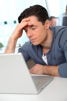 Office worker with exhausted look in front of computer