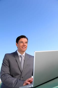 Smiling businessman working outside with laptop computer