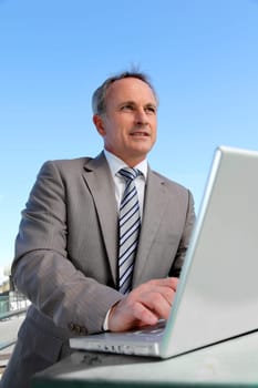Smiling businessman working outside with laptop computer