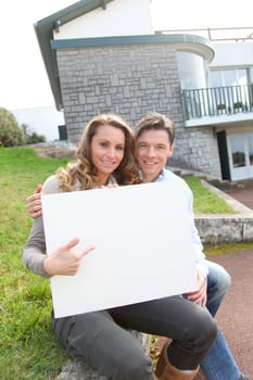 Couple holding whiteboard in front of their house