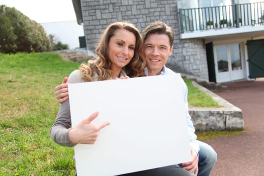 Couple holding whiteboard in front of their house