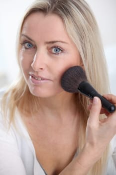 Beautiful blond woman applying makeup on her face