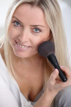 Beautiful blond woman applying makeup on her face