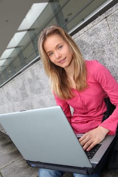 Student with laptop computer sitting outside school building