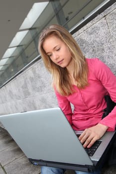 Student with laptop computer sitting outside school building