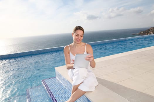 Woman using electronic tablet by swimming pool