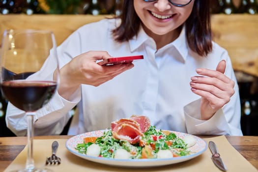 Happy woman in a restaurant taking pictures of food with a smartphone. Lifestyle, photo for social networks, personal blog concept