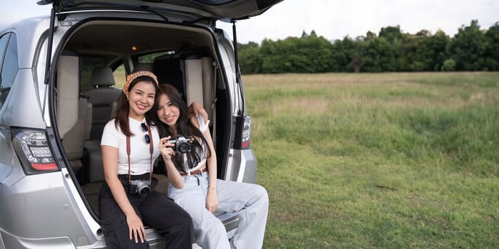 Car road trip travel couple tourists enjoying mountain view relaxing on car. Happy Asian woman, women friends smiling on car.