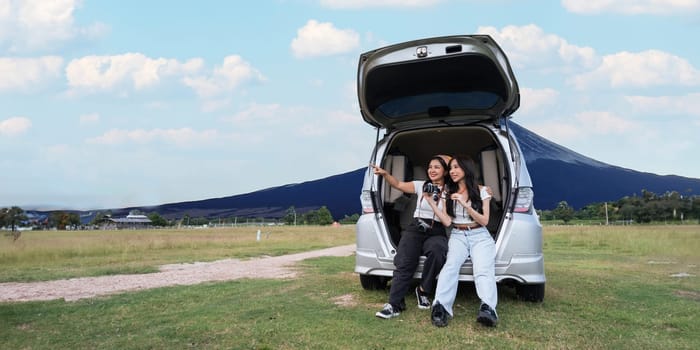 Car road trip traveling couple tourists enjoying mountain view relaxing on car. Happy Asian woman, women girlfriends smiling on car.