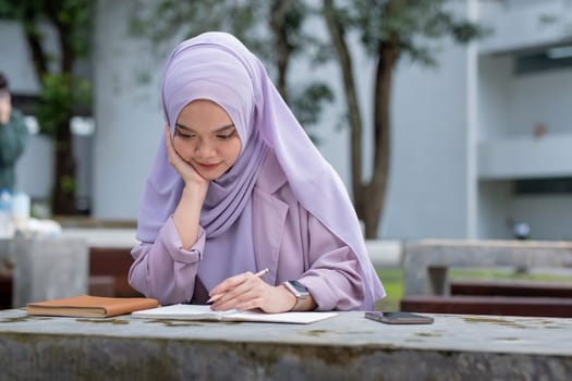 Beautiful Muslim college student girl taking note at university.