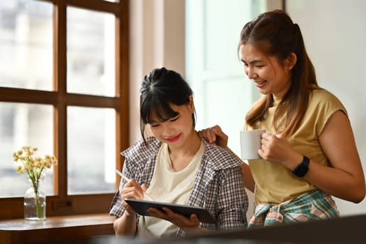 Two young woman using digital tablet and having a discussion during a coffee break in office.