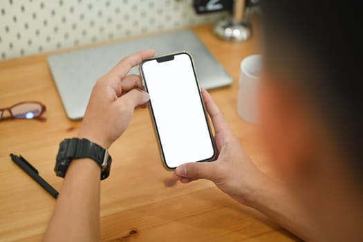 Close up male hands using smartphone at working desk searching data or chatting online.