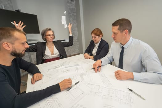 Four business people sitting around a table discussing blueprints. Designers engineers at a meeting