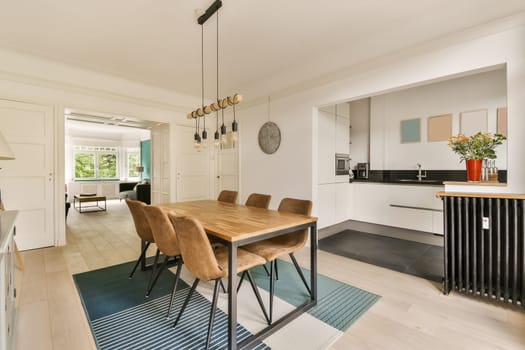 a kitchen and dining area in a house with white walls, hardwood flooring and light wood table surrounded by chairs