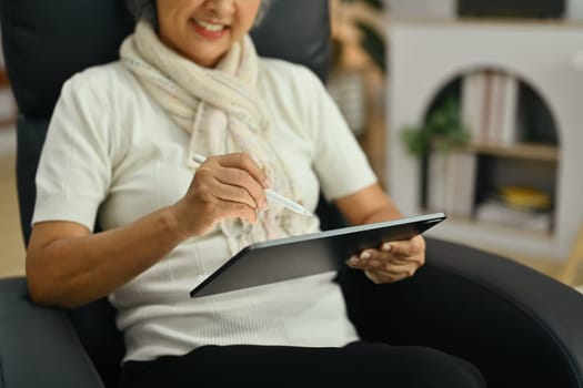 Happy middle age woman using digital tablet on comfortable armchair. People and technology concept.