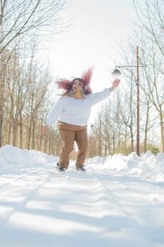 Smiling plump redhead woman jumping in park in winter