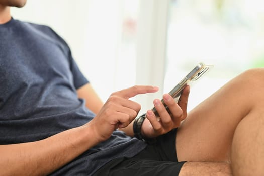 Young man sitting on couch and using smartphone, typing message or posting in social media.
