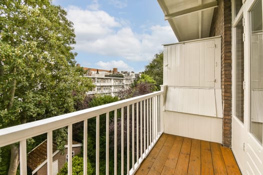 a balcony with wooden flooring and white railings on the side of a house, surrounded by lush green trees