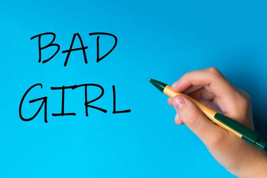 Children hand with pen write on a blue white background. Writing hand. Words Bad girl