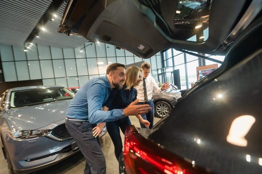 The seller demonstrates the interior of the car to buyers. Caucasian couple chooses a car