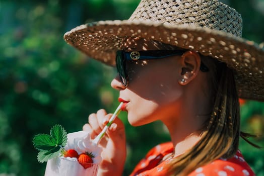 Pretty woman drinking strawberry milkshake cocktail with straw, nature backdrop. High quality photo