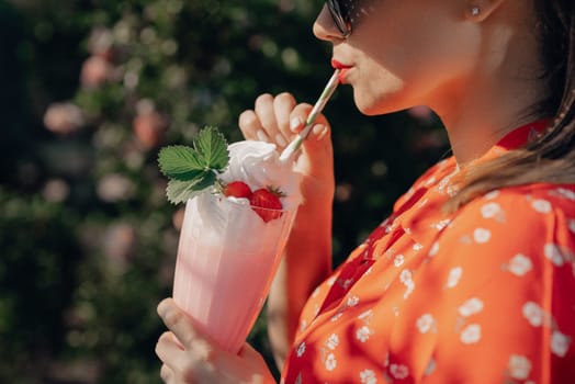 Pretty woman drinking strawberry milkshake cocktail with straw, nature backdrop. High quality photo