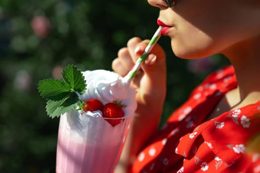 Pretty woman drinking strawberry milkshake cocktail with straw, nature backdrop. High quality photo