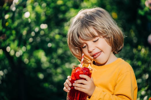 Cute little toddler boy with strawberry lemonade with straw, nature backdrop. High quality photo