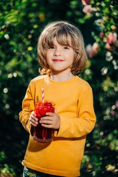 Cute little toddler boy with strawberry lemonade with straw, nature backdrop. High quality photo