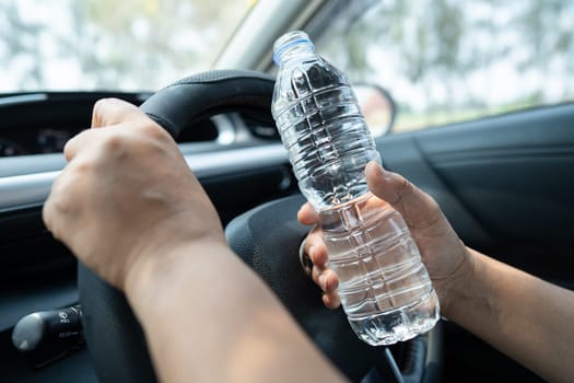 Asian woman driver holding bottle for drink water while driving a car. Plastic hot water bottle cause fire.