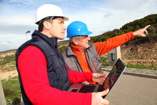 Construction workers with laptop computer looking at building