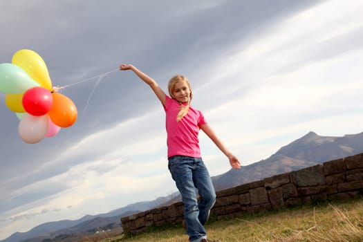 Little girl holding balloons out in the countryside