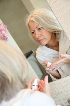 Senior woman applying moisturizer on her face