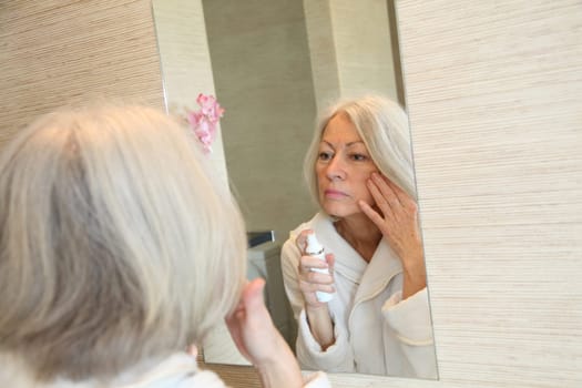 Senior woman applying moisturizer on her face